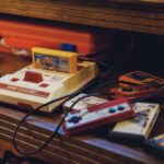 Vintage Nintendo Family Computer console on a wooden shelf with colorful game cartridges and red controllers scattered nearby.