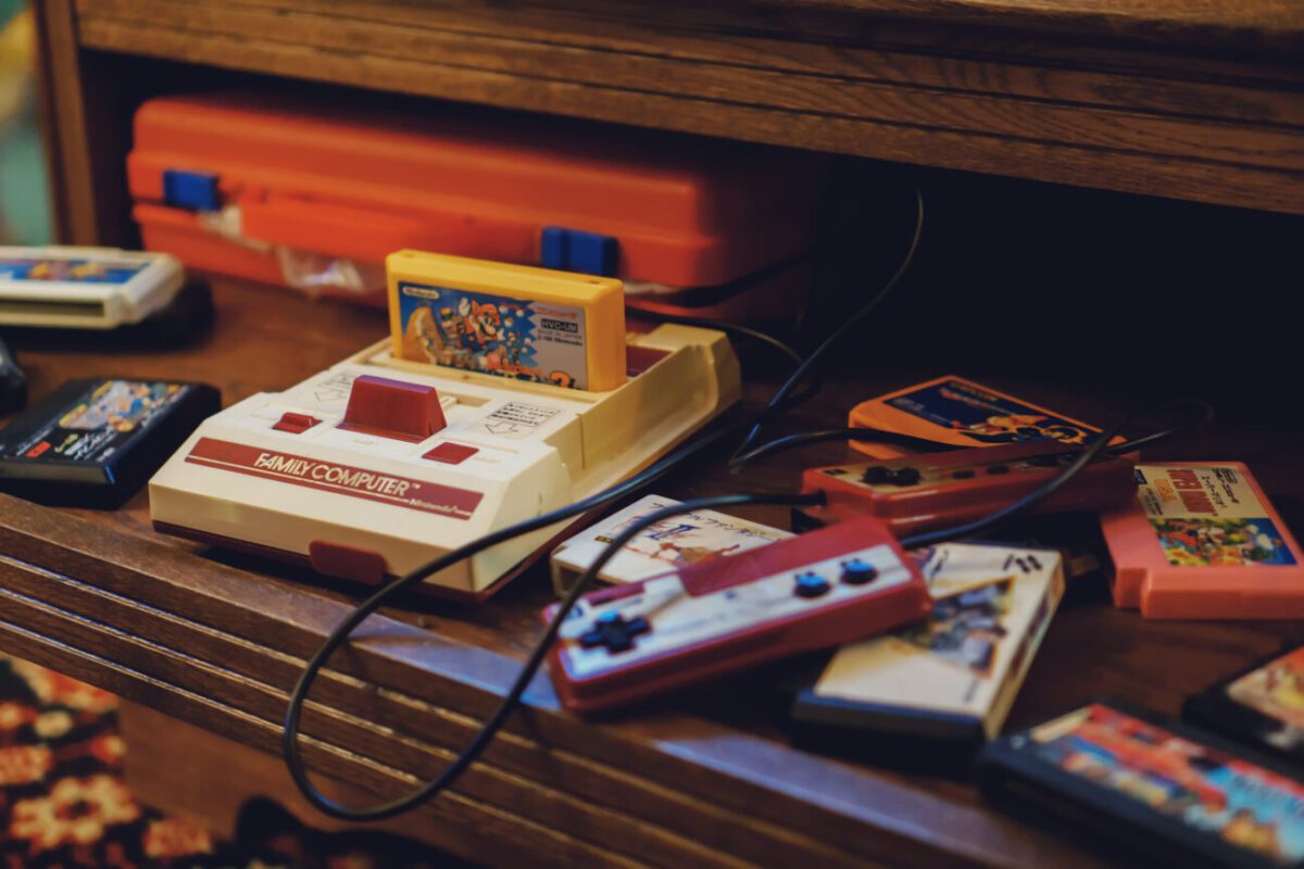 Tallinn Estonia - 21052022 LVLup Video Game Museum - Nintendo | 49k Noticias Vintage Nintendo Family Computer console on a wooden shelf with colorful game cartridges and red controllers scattered nearby.